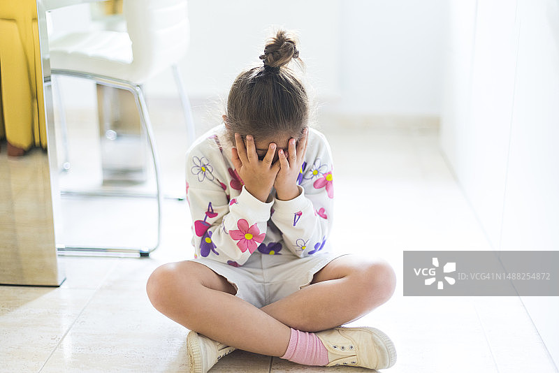 女孩坐在地板上，沮丧和愤怒地用手捂住脸。童年、心理健康概念图片素材