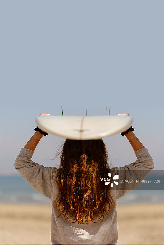 在沙滩上拿着冲浪板的年轻女人图片素材