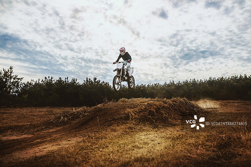 在蓝天下骑泥地摩托车的年轻男人图片素材