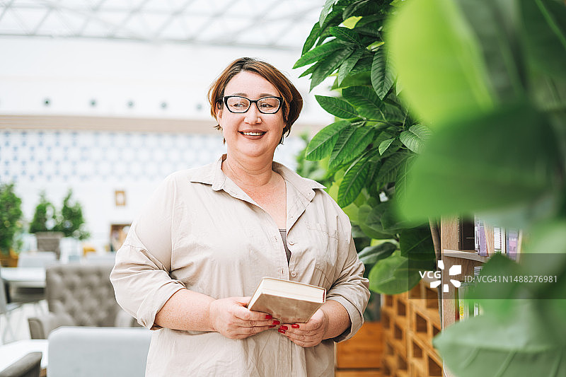 戴眼镜、穿着休闲的中年妇女在图书馆看书图片素材