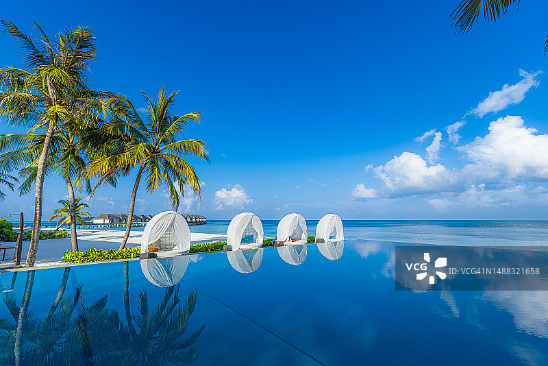 热带海滩酒店度假村的豪华遮阳伞和椅子，椰子树在泳池边，夏季旅游度假背景概念图片素材