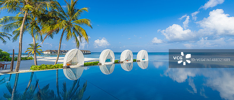 热带海滩酒店度假村的豪华遮阳伞和椅子，椰子树在泳池边，夏季旅游度假背景概念图片素材