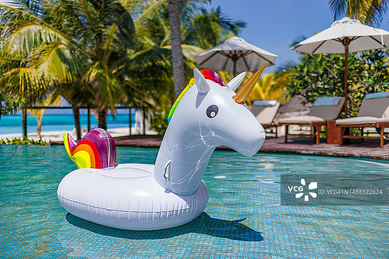 漂浮在阳光明媚的游泳池中的充气独角兽，热带豪华度假村家庭夏季放松概念，棕榈树和阳光明媚的热带海滩泳池，享受无忧无虑的娱乐活动图片素材