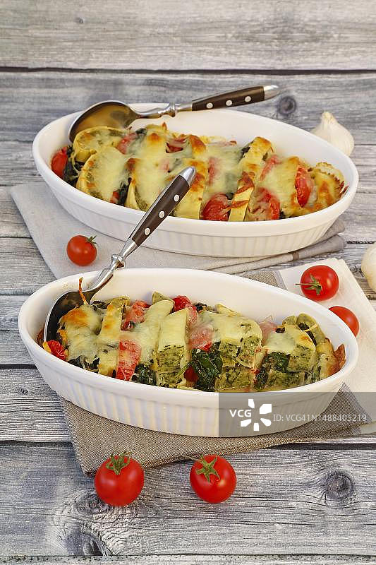 施瓦本美食：奶酪焗Maultaschen，烤箱烤制的肉馅意大利面片，融化的奶酪，番茄片，菠菜分层放在砂锅菜中，樱桃番茄，鸡尾酒番茄，勺子，传统美食，食品摄影图片素材