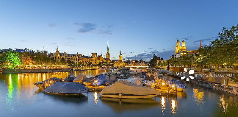瑞士苏黎世老城区的利马特河、圣母大教堂和格罗斯大教堂的傍晚景色，以及港口和船只图片素材