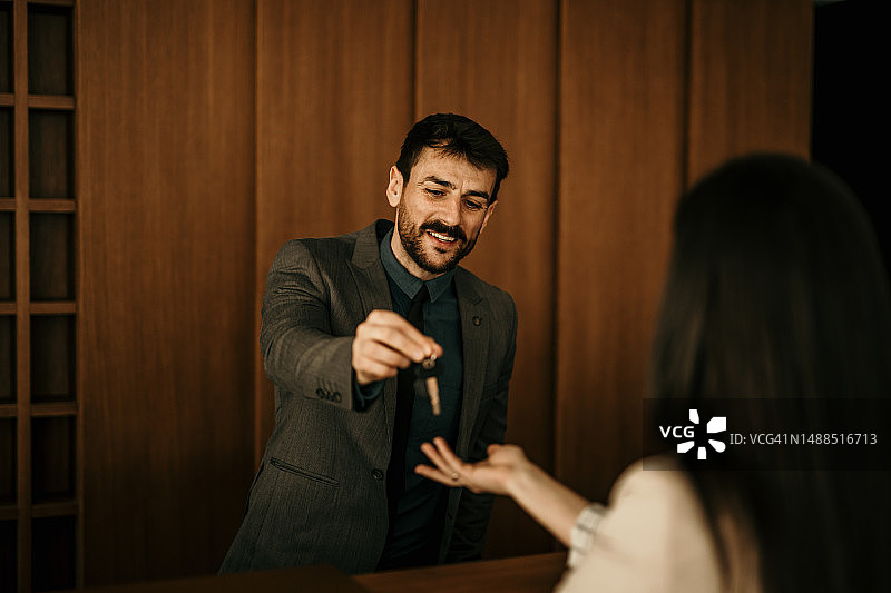 男接待员与正在办理入住手续并递给她钥匙的酒店客人交谈图片素材