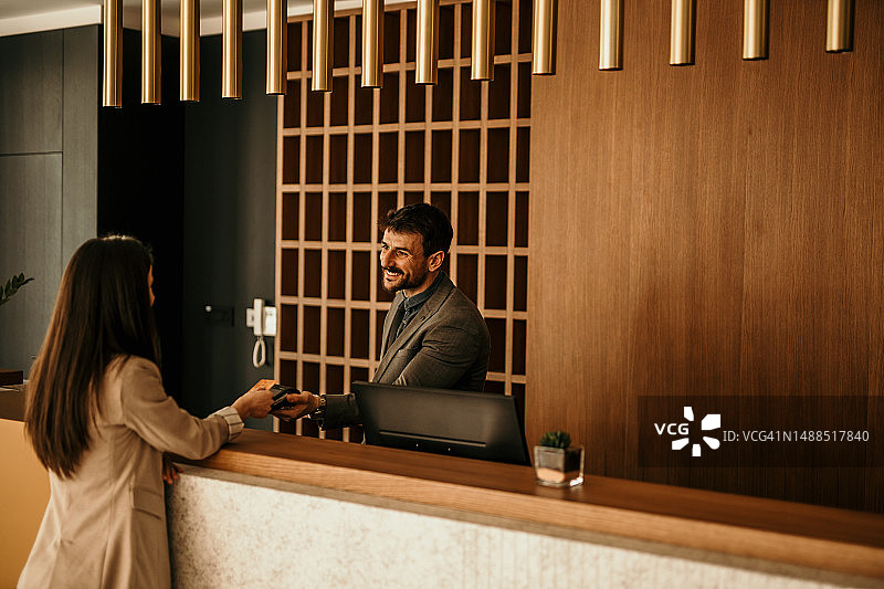 微笑的酒店接待员在前台为女客人服务，礼宾员将文件交给客人图片素材
