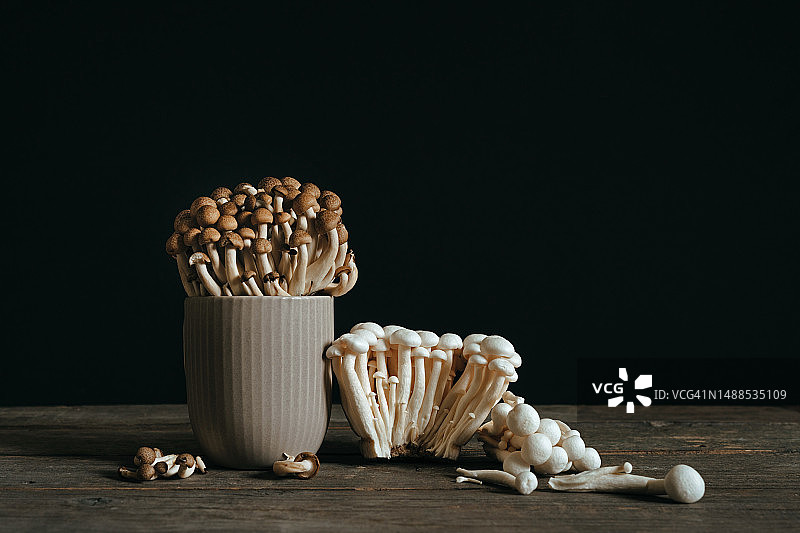 黑色背景下木桌上灰色杯子里的棕色和白色白玉菇图片素材