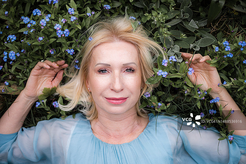 身穿浅蓝色衬衫的老年妇女在草地上与鲜花合影图片素材