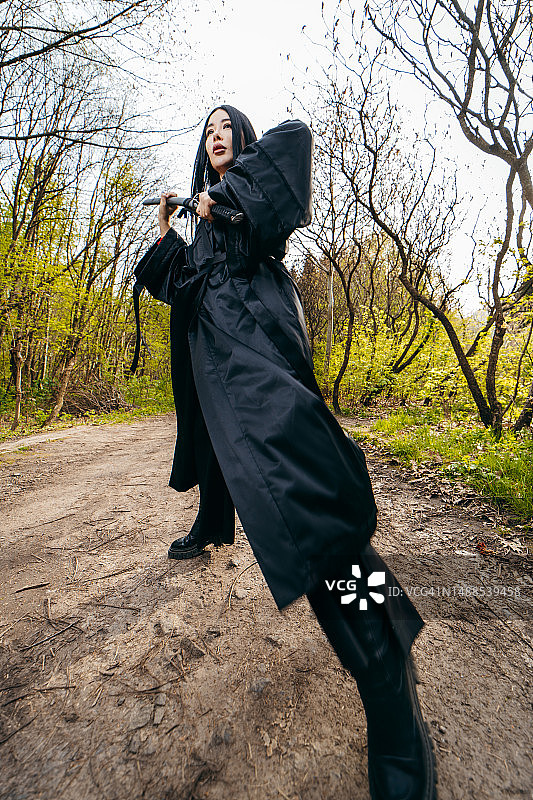 身穿黑色传统和服、手持武士刀的年轻亚洲女孩，背景为自然风光图片素材