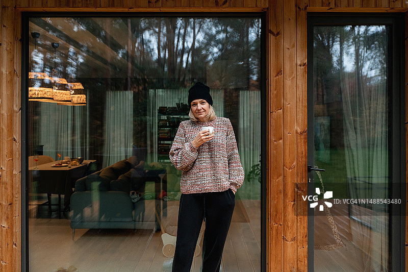 中年妇女在木屋外喝热饮图片素材