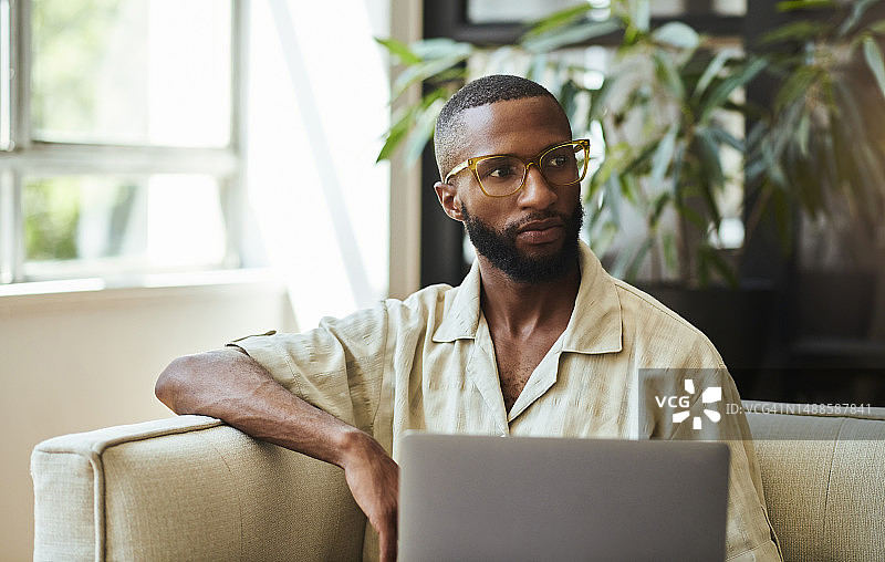坐在沙发上的年轻黑人男子，戴着眼镜，目光离开相机图片素材