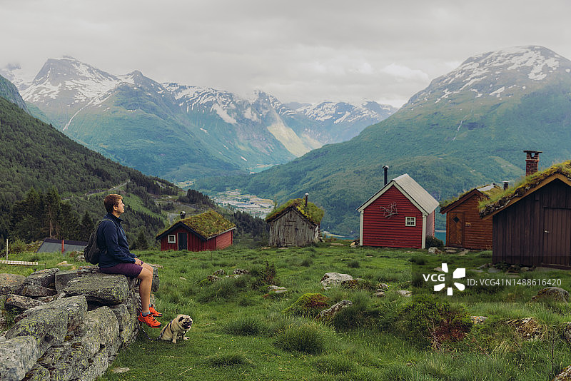 男人和狗在挪威欣赏山谷和木屋的侧面像图片素材