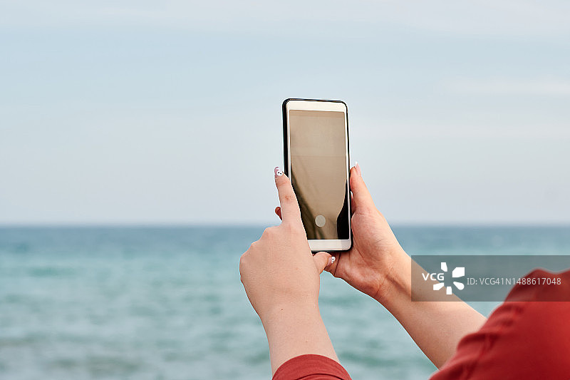 一个人拿着手机，背景是海图片素材