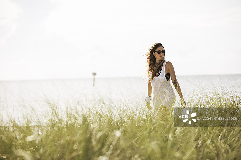一位迷人的女性走在岸边，前景是长长的草图片素材