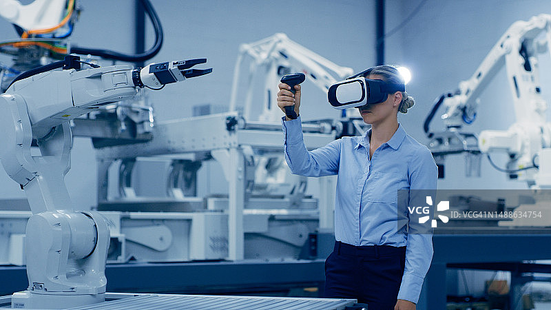 工业4.0中用于人工智能、未来电子产品和制造的机器人、VR眼镜和使用操纵杆的工程女性。 机器人手臂、车间和具有虚拟现实和机器的技术人员图片素材