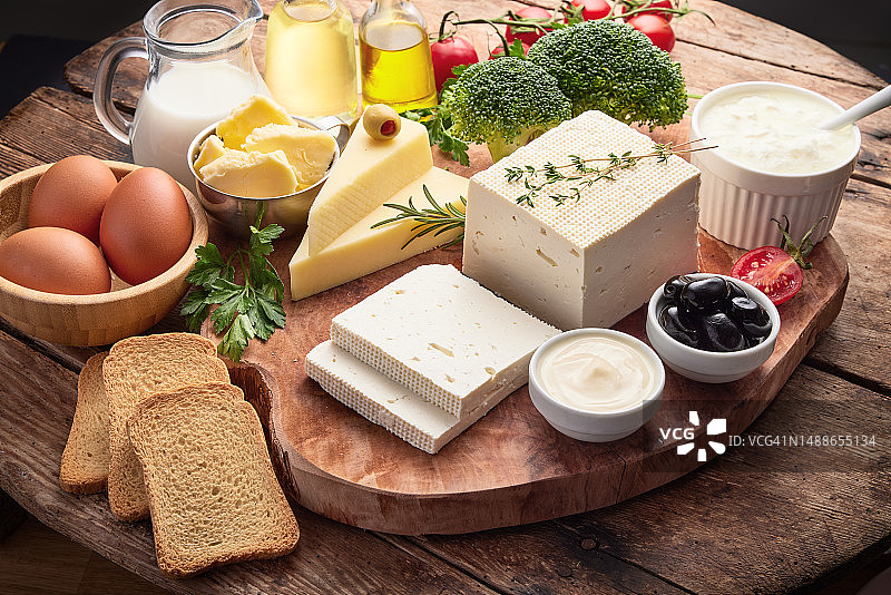 木制背景上的新鲜乳制品，牛奶、奶酪、黄油、鸡蛋、蔬菜、香草、面包的食物拼贴图片素材