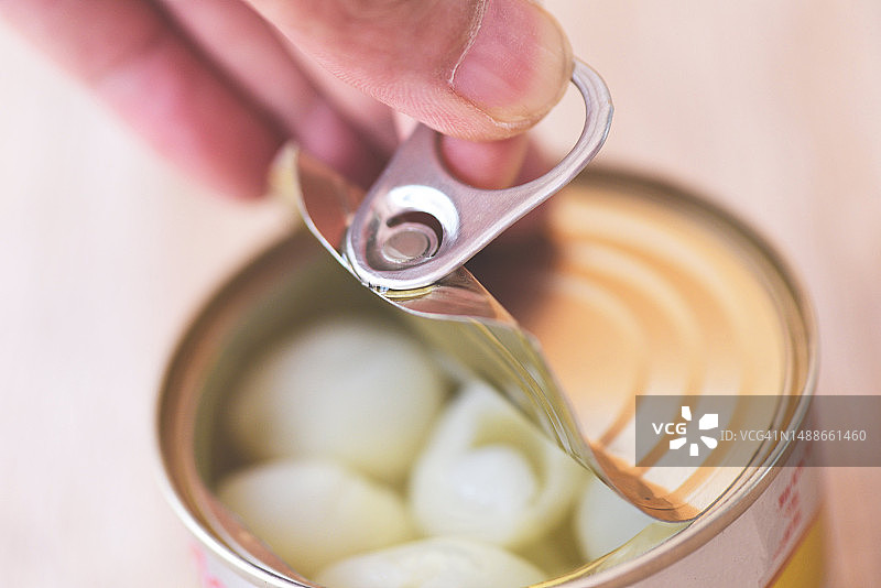 手打开木质背景上的金属罐头食品，特写：厨房中不易腐烂的食品储藏品，龙眼罐头水果，罗马尼亚图片素材