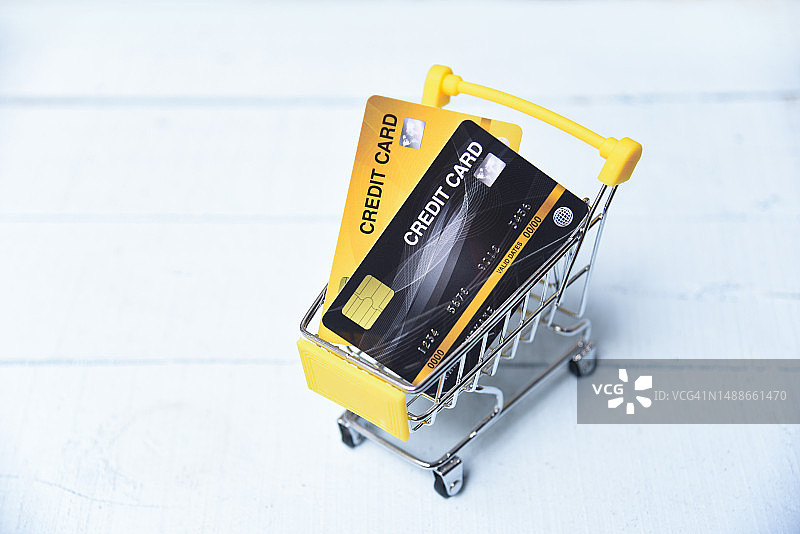 在木制背景上手持信用卡在购物车中在线购物，用于在家在线支付图片素材