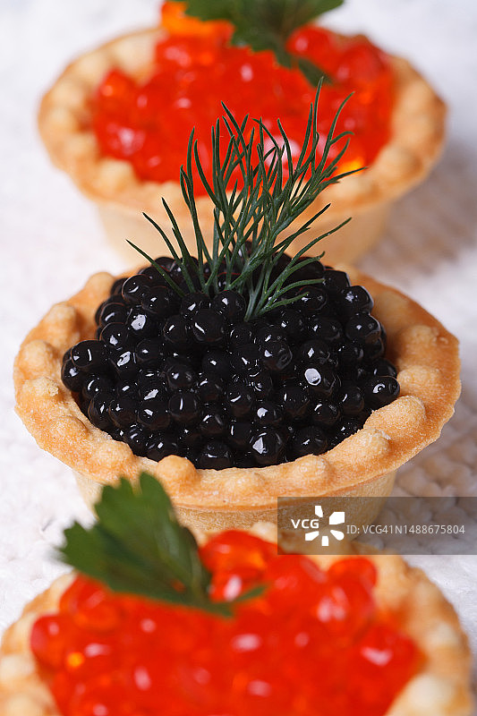 三个红色鲑鱼子酱和鲟鱼子酱黑色小馅饼特写，竖版图片素材