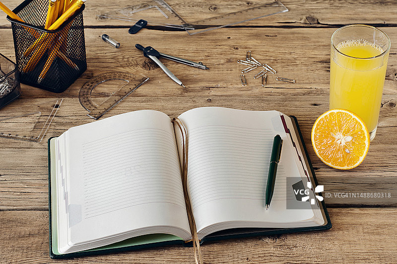 木桌上放着一杯新鲜橙汁和办公用品的空白记事本图片素材