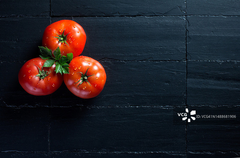 黑色石板上三个新鲜多汁的西红柿特写，带文案空间图片素材