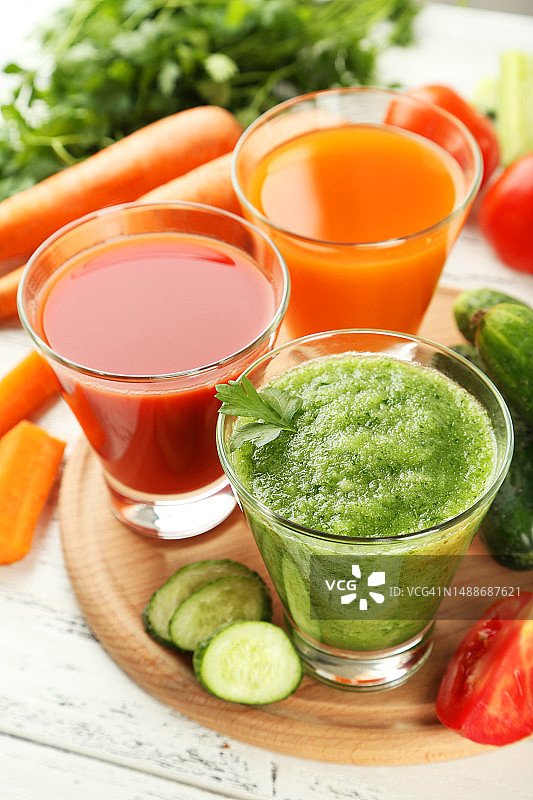 白色木质背景上的新鲜番茄、胡萝卜和黄瓜汁图片素材