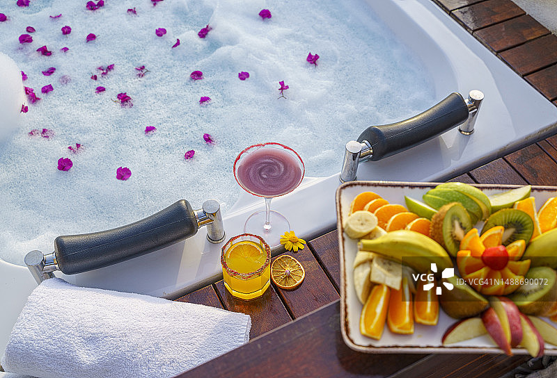 屋顶水疗浴缸旁的泳池鸡尾酒和水果拼盘图片素材