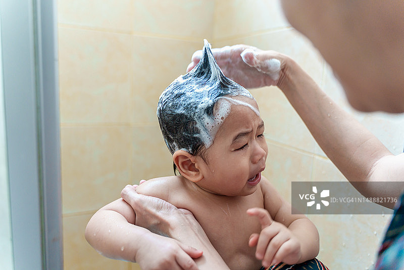 年轻可爱的亚洲男婴在洗澡和洗头时哭泣。婴儿的日常护理、卫生和亲子关系概念。父母在家照顾婴儿。家庭生活方式和亲子关系概念。图片素材