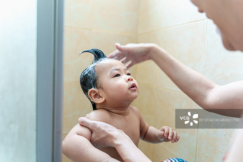 父母在浴室为可爱的幼儿宝宝洗头发，可爱的亚洲新生婴儿享受沐浴放松，父母在家照顾婴儿，家庭亲子生活方式图片素材