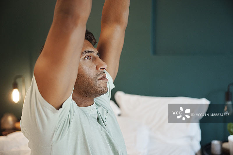 男子夜晚在床上伸展双臂：睡眠、休息与疲惫图片素材