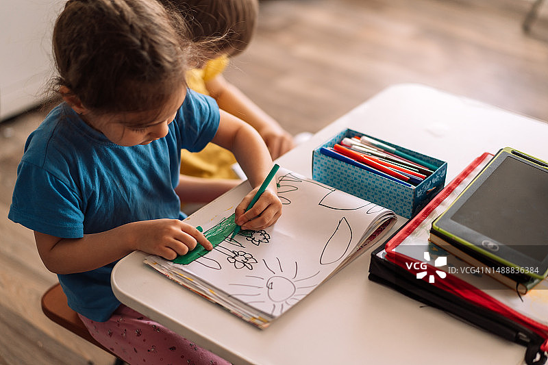 在白色课桌旁的教室里，用毡尖笔在画册上绘画的学生，重返校园的概念图片素材
