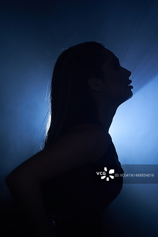 舞台烟雾中身穿黑色摇滚套装的美丽年轻女子轮廓图片素材