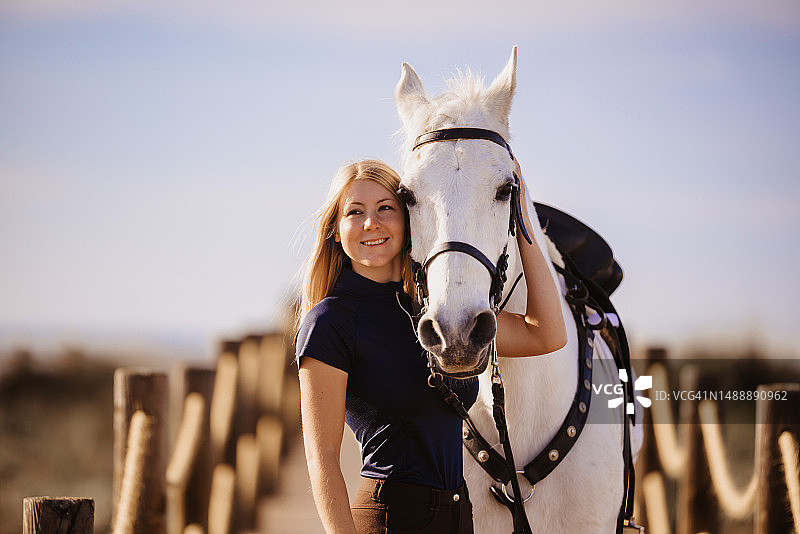 拥抱白色骏马的年轻金发女子肖像图片素材