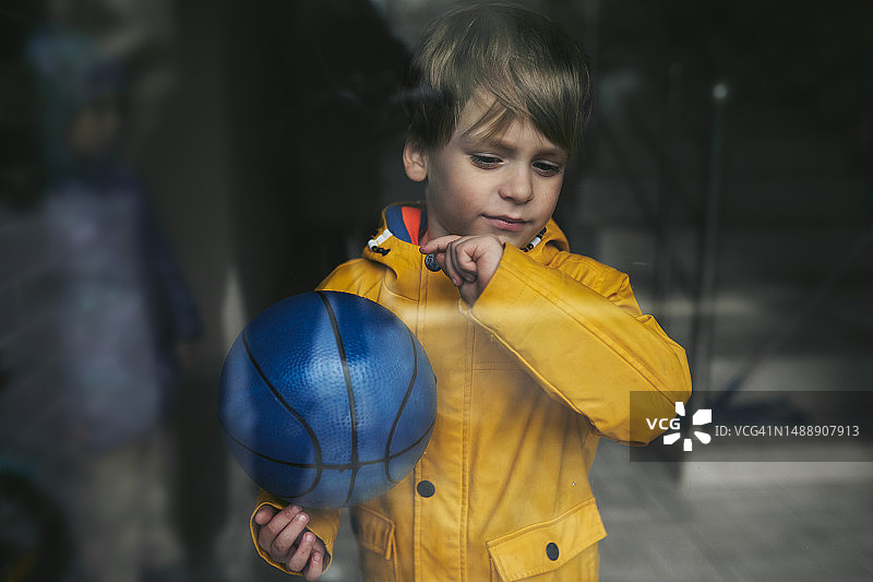 穿着黄色夹克抱着蓝色球的悲伤的4岁男孩的肖像图片素材