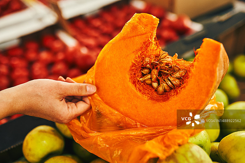 市场柜台上蔬菜水果背景下的橙色南瓜和一只女人的手图片素材