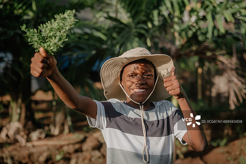 站在牙买加植物前，拿着帽子的男孩肖像图片素材