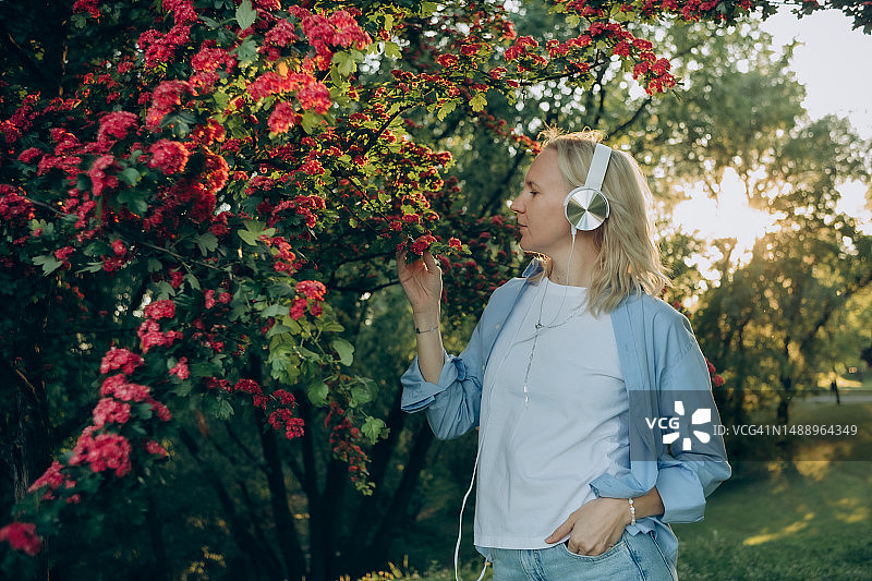 金发女子在开花的树下戴着耳机图片素材