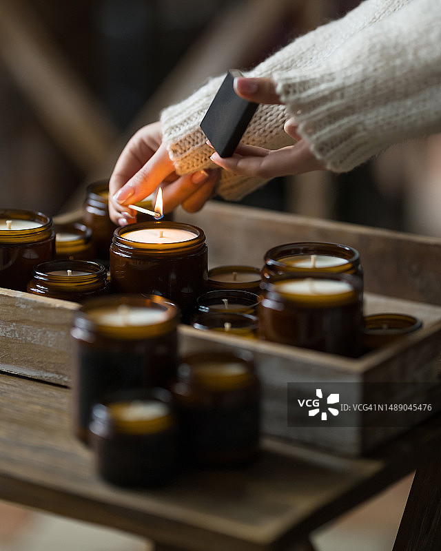 女人点燃蜡烛。女人手中燃烧的火柴。棕色罐子里的香味手工蜡烛。芳香疗法，水疗，放松。家庭舒适。侧视图。柔焦图片素材