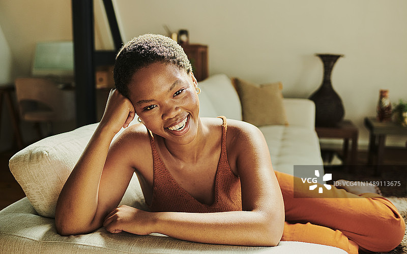 快乐的年轻黑人妇女坐在舒适的客厅沙发上。来自南非的年轻女性在休息室的沙发上放松身心，拥有复制空间图片素材