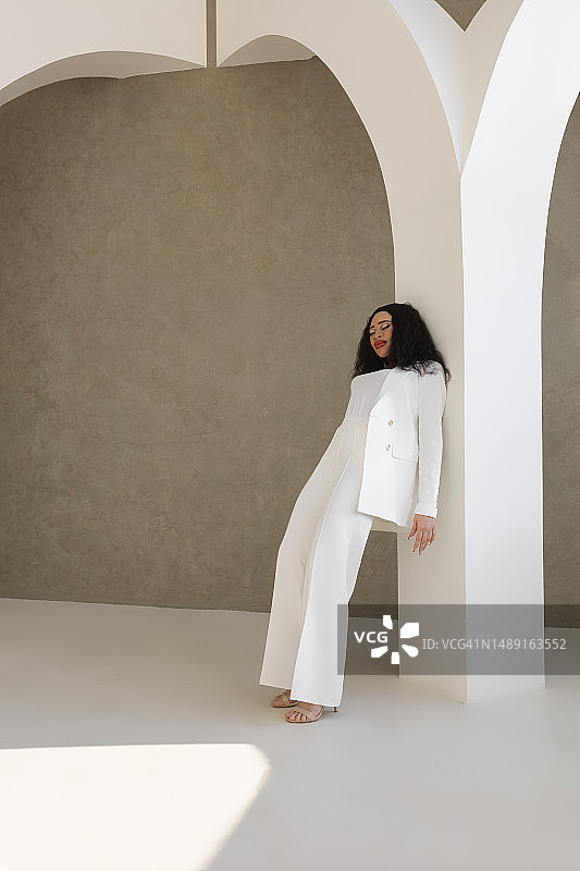 身穿白色西装倚靠白色柱子的迷人黑发女子图片素材