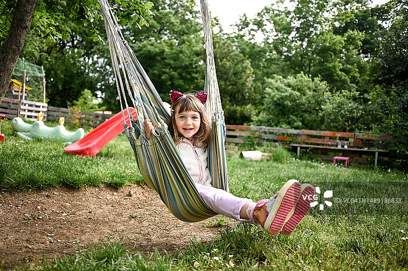 戴着猫耳朵的可爱学龄前女孩在花园吊床上玩耍的肖像图片素材