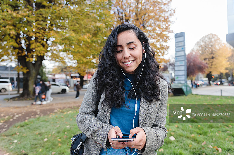 在城市草地上漫步的年轻拉丁裔高管正在使用手机图片素材