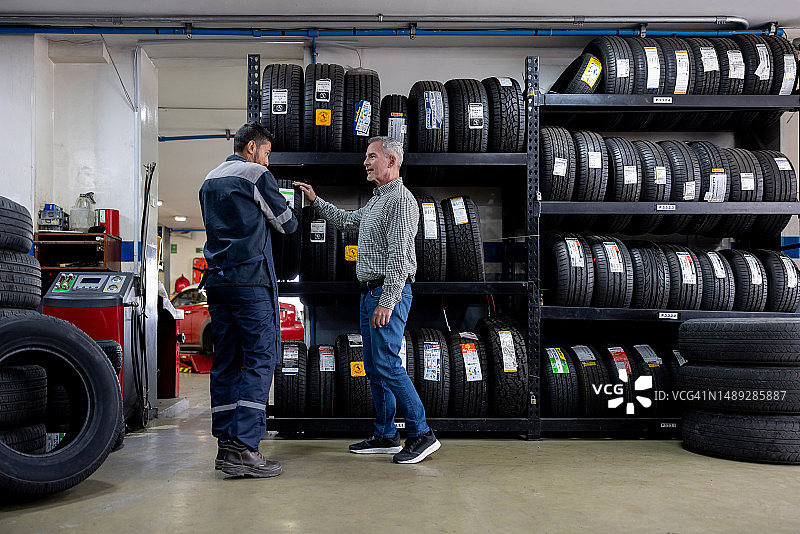男人更换汽车轮胎并与修理工交谈图片素材