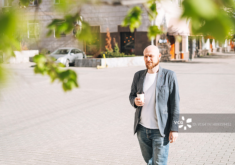 成年男人身穿蓝色西装，手拿纸杯咖啡走在城市街道上图片素材