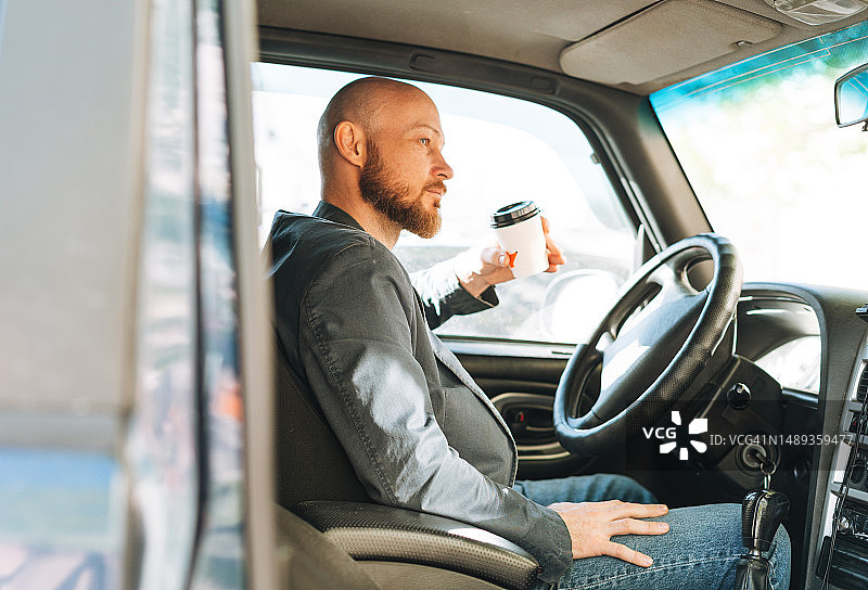 成年男子穿着蓝色西装，拿着咖啡纸杯在城市里开车图片素材