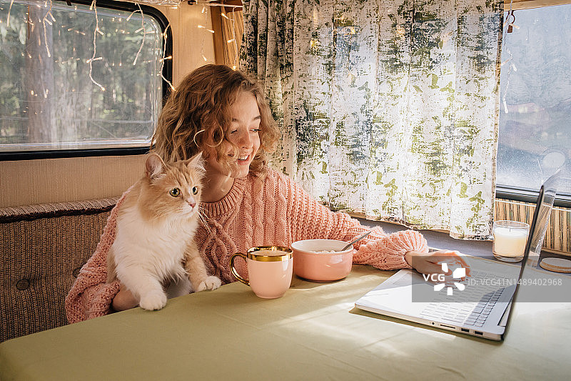 女人和小姜猫在拖车里边吃早餐边看笔记本电脑图片素材