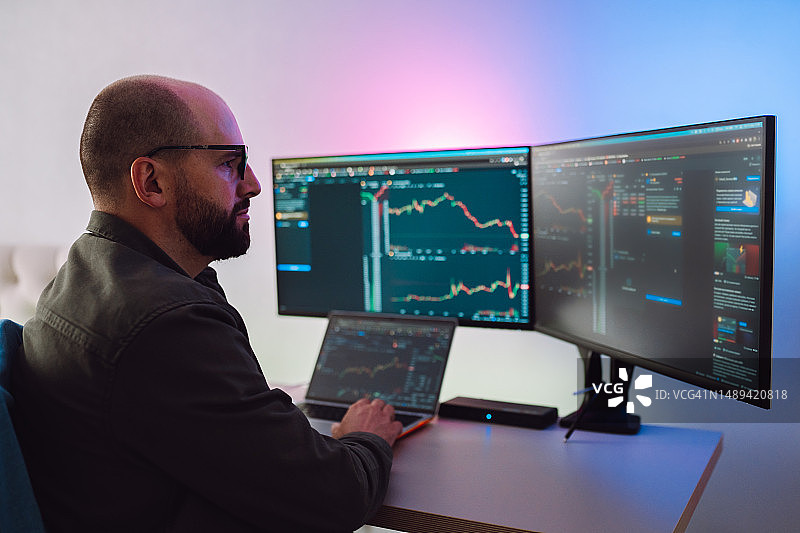 戴眼镜的严肃男金融顾问在家办公，查看屏幕上的交易软件图片素材