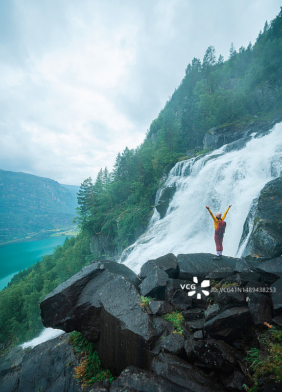 在挪威山区瀑布附近举起双臂的女人图片素材