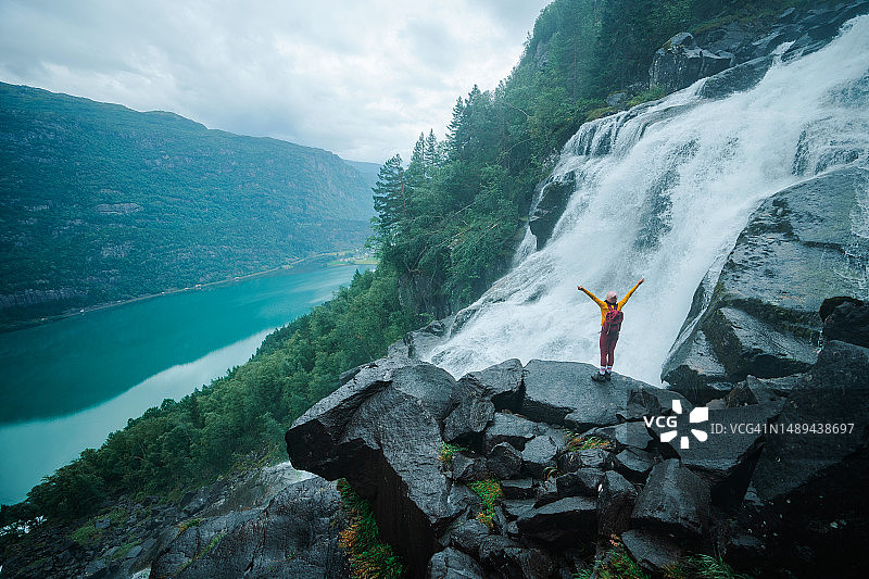 在挪威山区瀑布附近举起双臂的女人图片素材